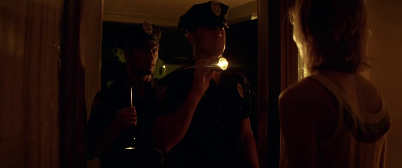 Magic Mike (2012) movie still: medium — Two police officers stand in a dark doorway holding flashlights directed at a woman. The beam of light hits…