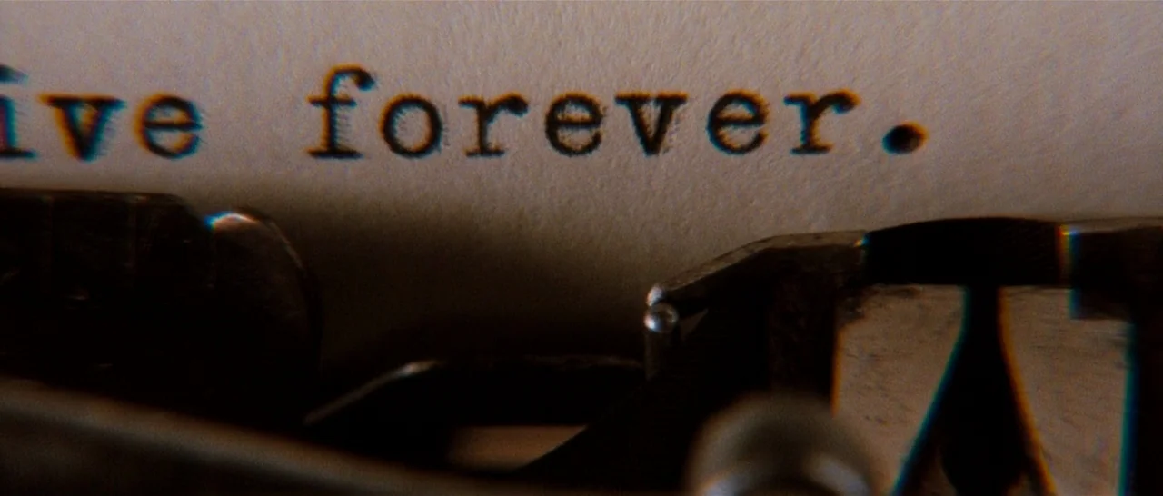 Moulin Rouge! (2001) movie still: closeup — A close-up view shows the phrase live forever typed onto an off-white paper sheet. The metal typebars…