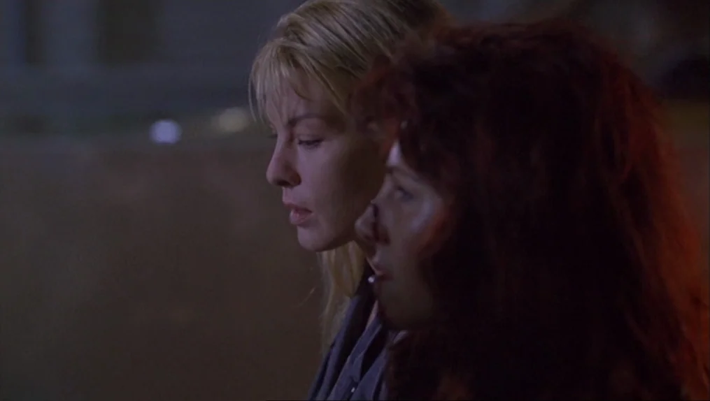 Crash (1996) movie still: medium — Two women stand in a dark outdoor setting at night. They are positioned in profile and look out of frame.