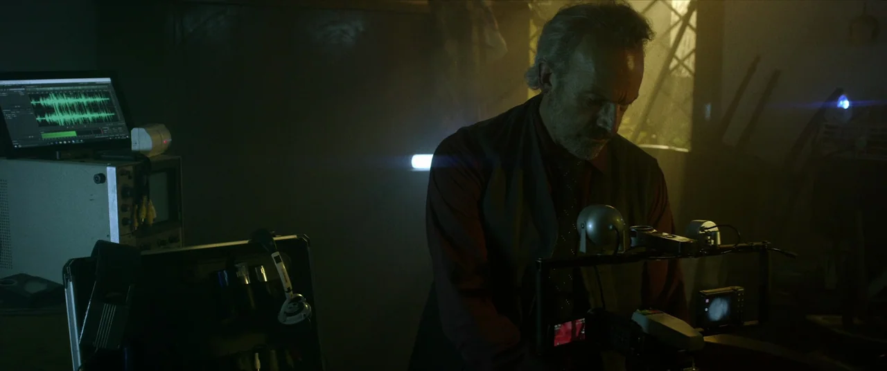 Terrified (2017) movie still: medium — A dark, dimly lit room filled with complex audio surveillance and recording hardware equipment. An older man…