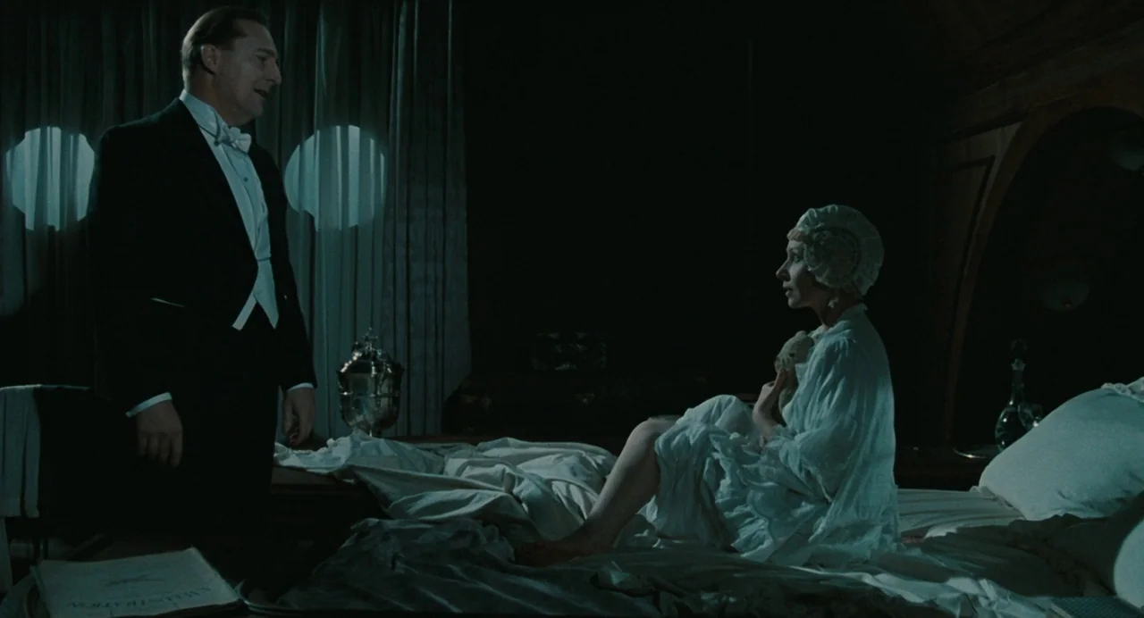 And The Ship Sails On (1983) movie still: medium — A dimly lit room with heavy curtains and a bed featuring white linens. A man in formal wear…
