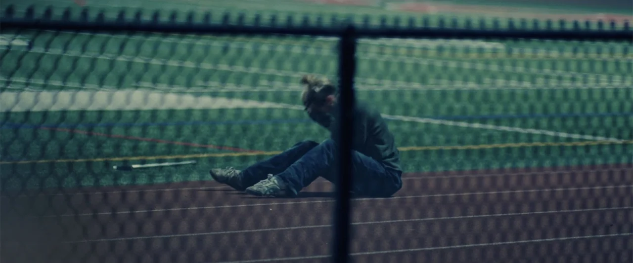 Chemical Hearts (2020) movie still: wide — A person sits on the rubber surface of a multi-lane athletic running track. The individual is positioned…
