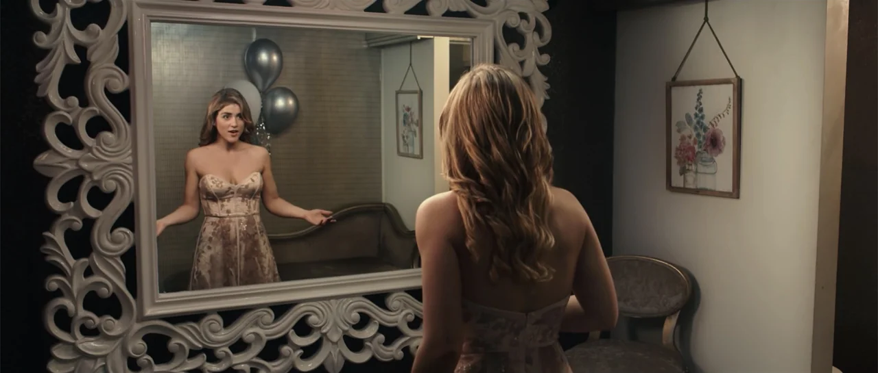 Cindy La Regia (2020) movie still: medium — A dressing room features a large white ornate mirror and a small wooden chair. A young woman stands…