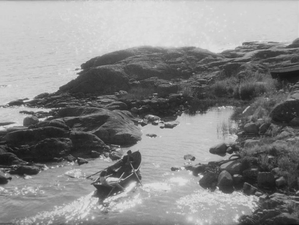 A Ship Bound for India (1947) movie still: wide — A rocky coastal shoreline features small tide pools and jagged grey stones. A couple in a wooden…