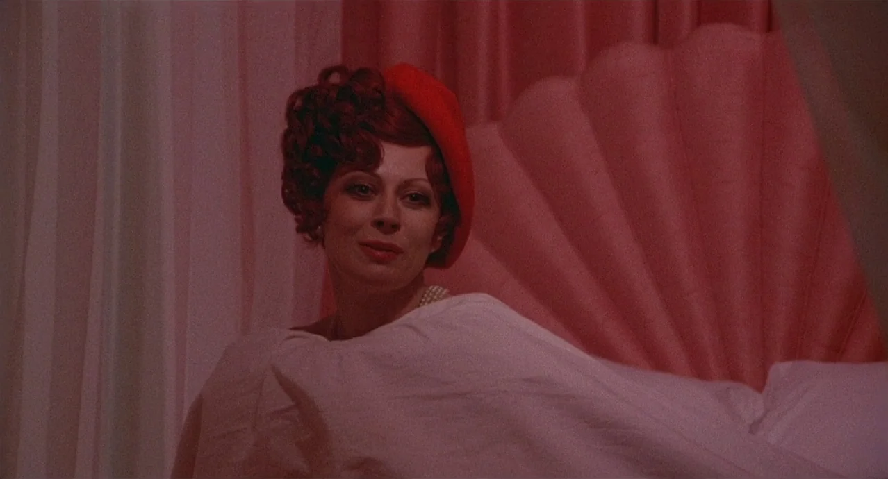 Amarcord (1973) movie still: closeup — A woman rests against a pink scalloped headboard in a dimly lit room. She wears a red beret and a pearl…