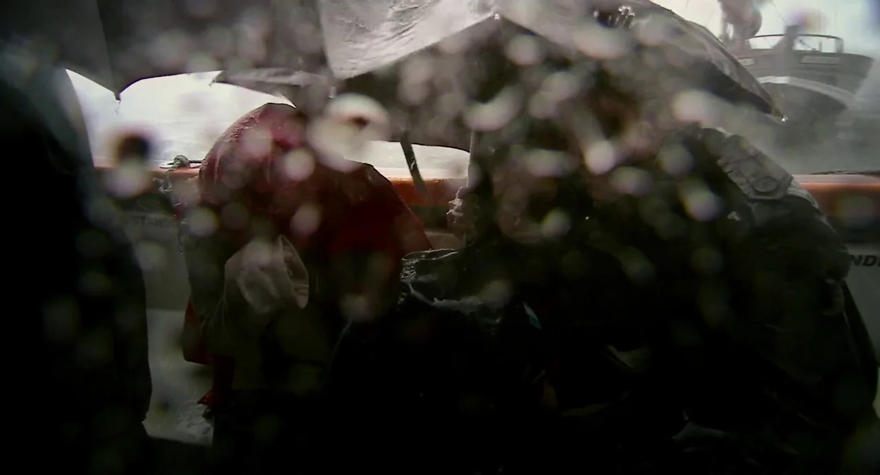Everyday (2012) movie still: medium — A small boat occupies rough water under heavy rain during a storm. Two people huddle beneath a black umbrella…