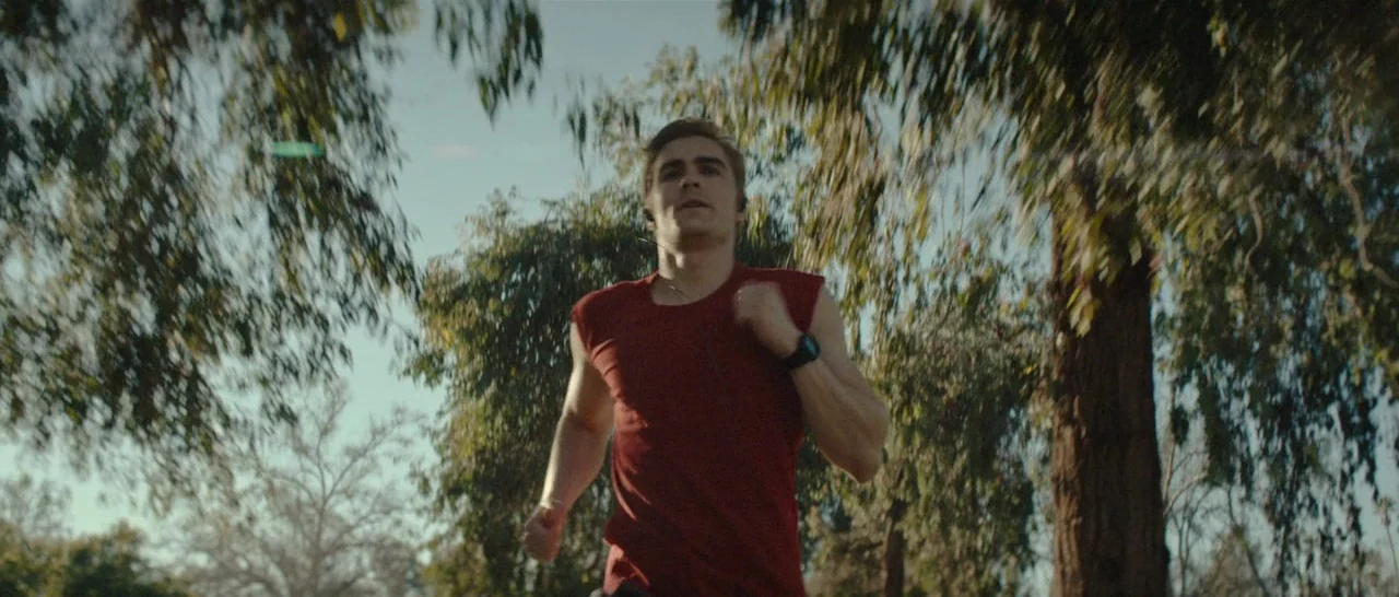 The Disaster Artist (2017) movie still: medium — A man jogs through a grove of eucalyptus trees with blurred foliage framing the shot. He wears a…