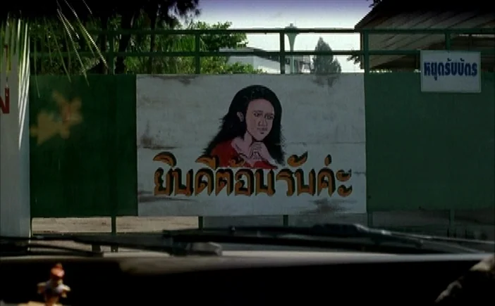 Blissfully Yours (2002) movie still: wide — A green metal gate displays a painted sign with a woman's portrait and text. The view is framed from…