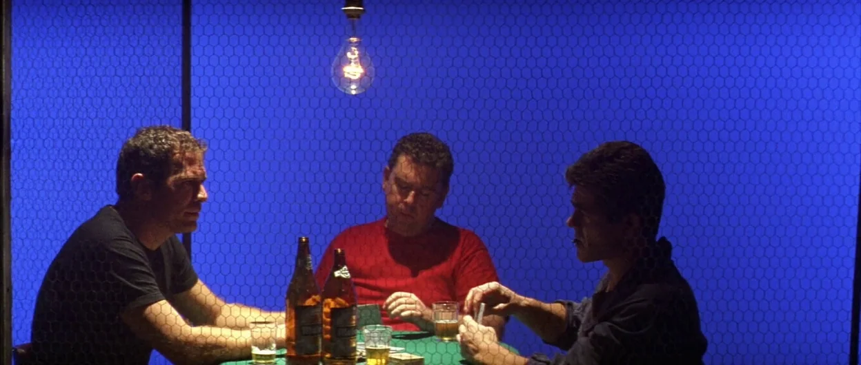 All About My Mother (1999) movie still: medium — Three men play cards at a small green table beneath a solitary hanging light bulb. A bright blue…