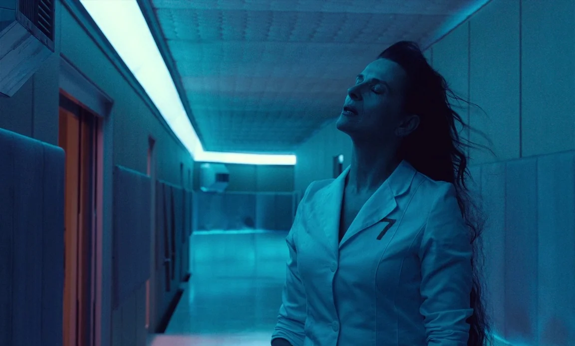 High Life (2018) movie still: medium — A sterile futuristic hallway with blue-tinted walls and ceiling lighting fixtures. A woman in a white coat…