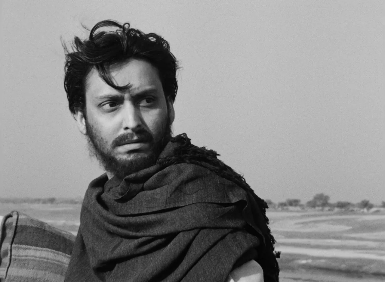 Apur Sansar (1959) movie still: medium — An open, flat, sandy landscape extends toward a hazy horizon under an overcast sky. A man with a dark beard…