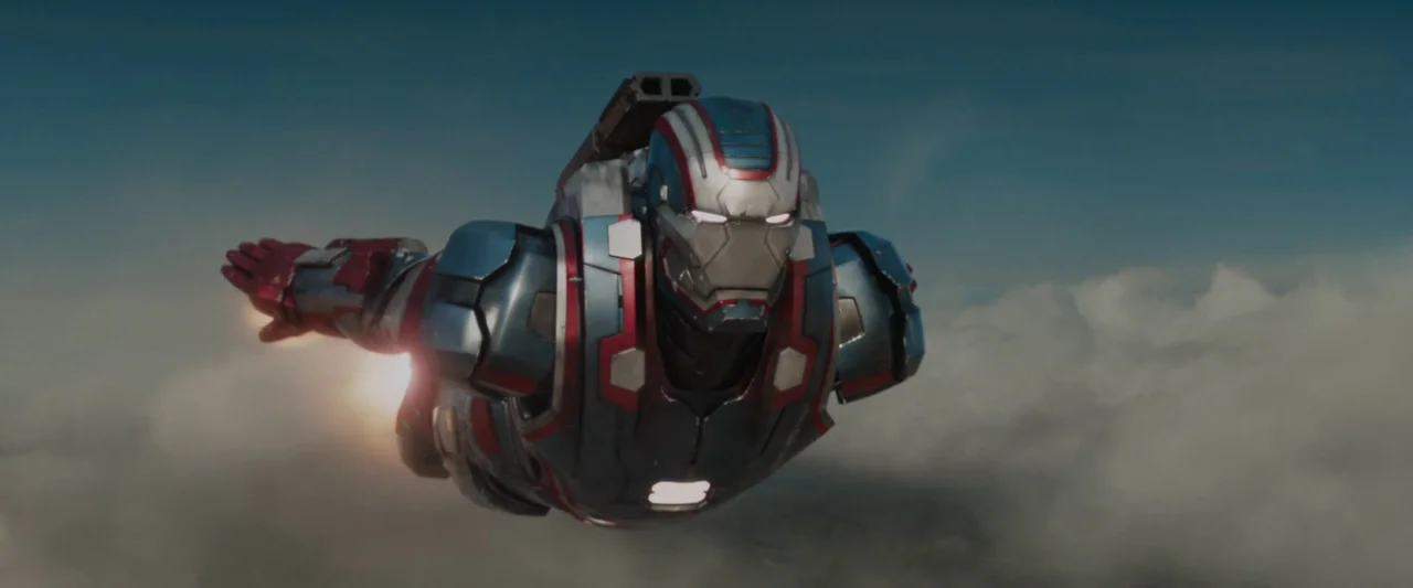 Iron Man 3 (2013) movie still: medium — A high-tech armored figure flies horizontally through the air above a dense cloud bank. The suit has red,…