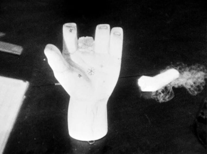 Fireworks (1947) movie still: closeup — A white palm-shaped sculpture stands on a dark, flat surface with small star symbols. A small, cloudy white…