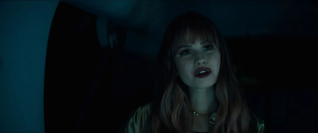 Night Teeth (2021) movie still: closeup — The inside of a car at night with dark surroundings and blue ambient lighting. A young woman with bangs…