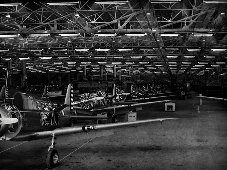 Saboteur (1942) movie still: establishing — An expansive industrial assembly hall features rows of partially completed propeller aircraft under…