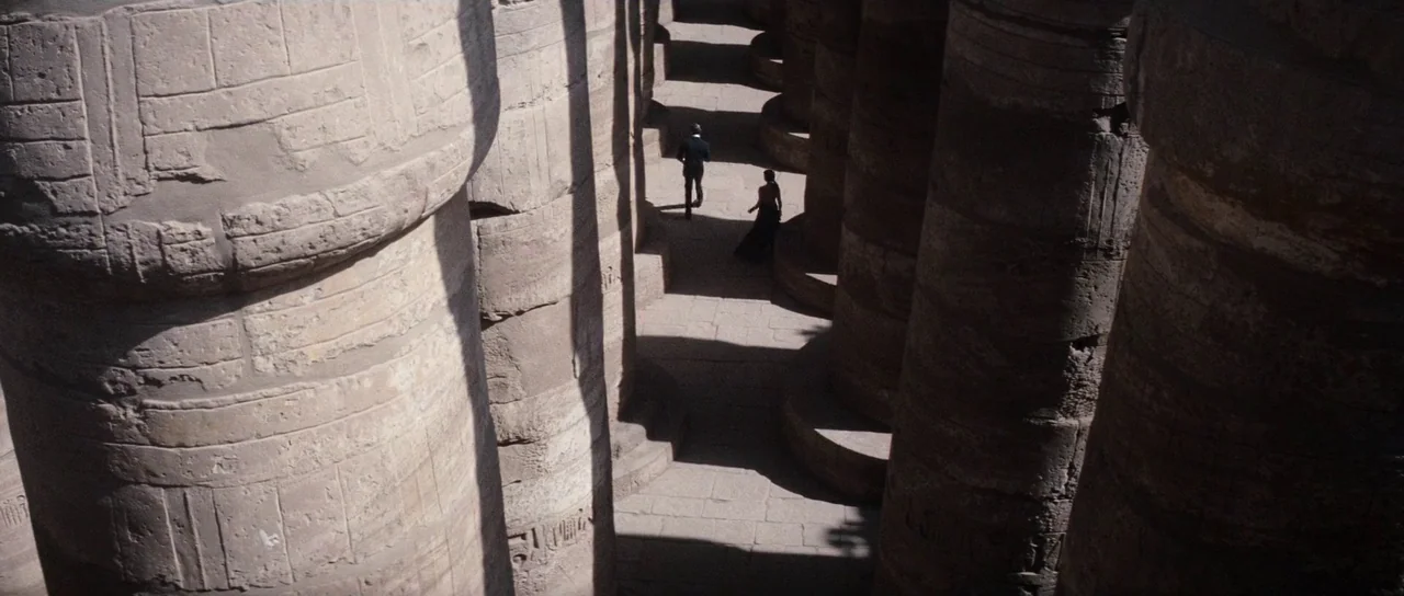 The Spy Who Loved Me (1977) movie still: wide — Massive ancient stone pillars line a narrow sandy walkway in an open-air site. A man and a woman…