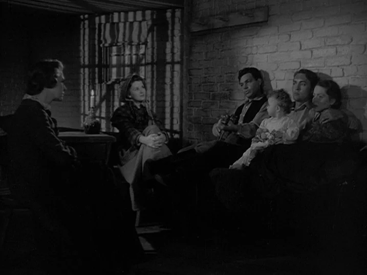 Young Mr. Lincoln (1939) movie still: wide — A rustic interior featuring white-washed brick walls and a dimly lit candle environment. A group of…
