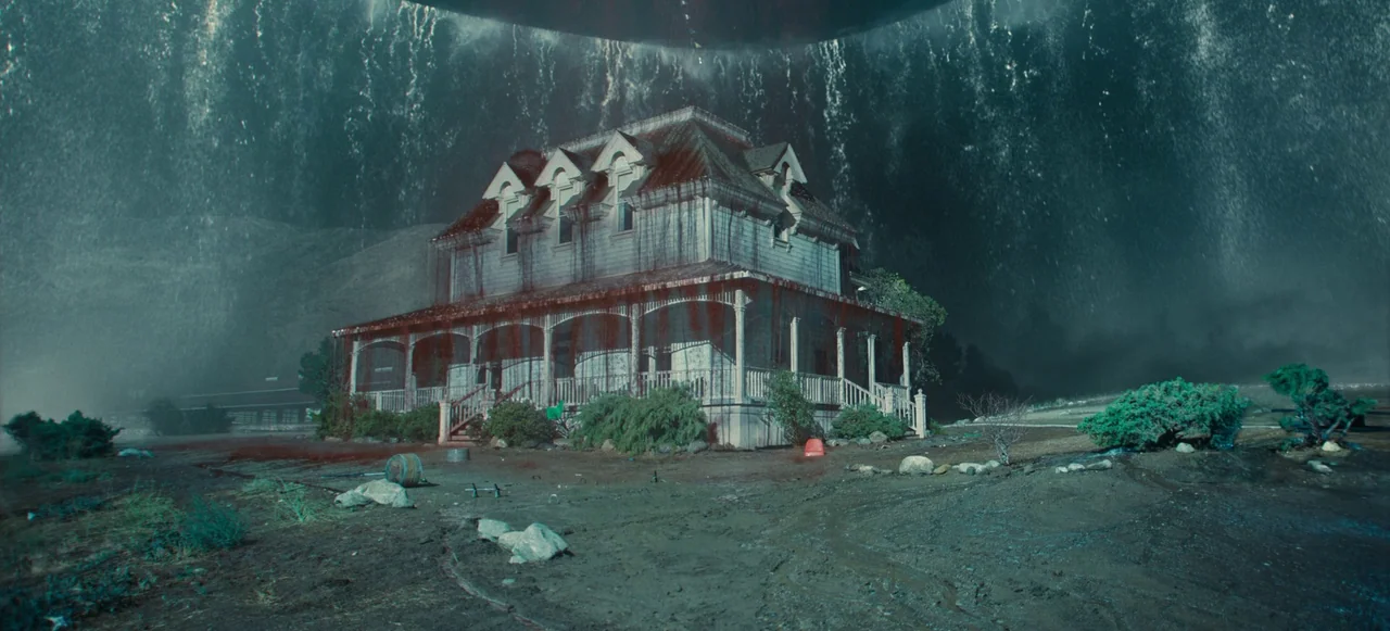 Nope (2022) movie still: wide — A two-story wood-frame farmhouse stands against a dark, storm-like backdrop with raining dark liquid. Deep red…