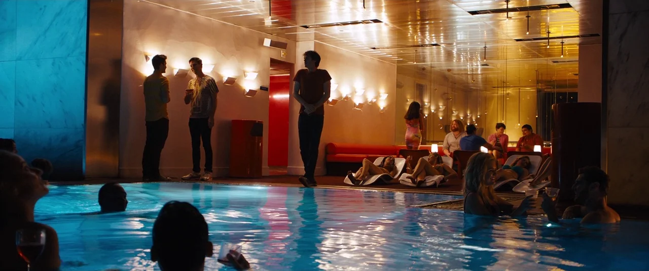 Under The Silver Lake (2018) movie still: wide — A modern indoor pool area features warm lighting fixtures and tiled walls with lounge seating.…