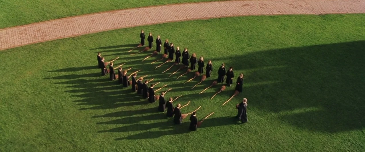 Harry Potter and the Philosopher's Stone (2001) movie still: wide — A group of students in dark robes stand in rows on a large lawn. They stand…