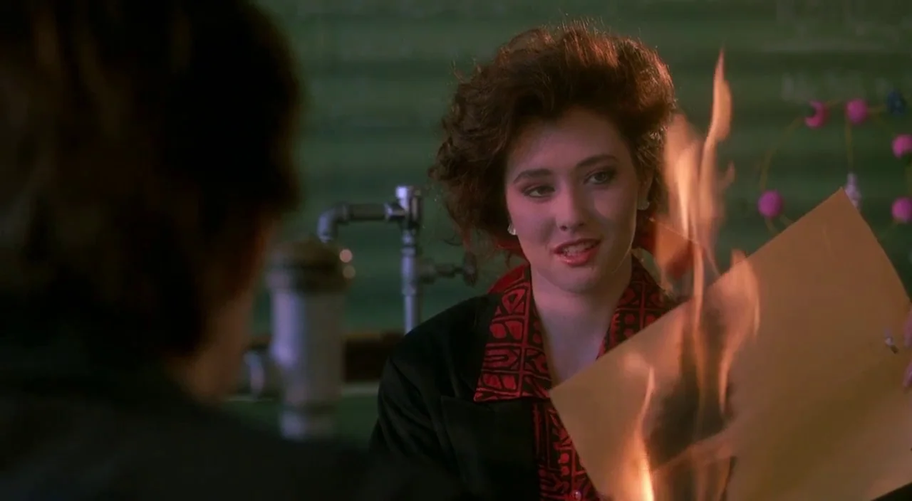 Heathers movie still: medium — A high school science laboratory contains green industrial cabinets and metal plumbing hardware. A young woman with…