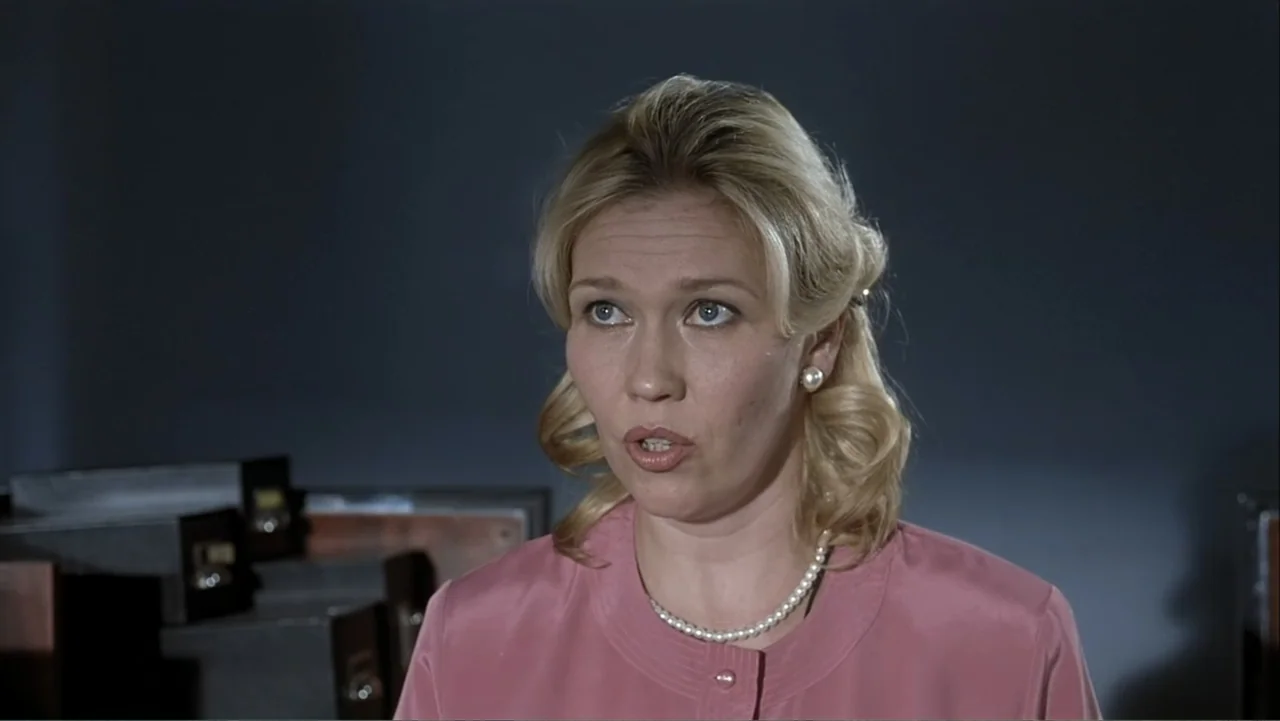 The Man Without a Past (2002) movie still: medium — A woman stands in a nondescript office with dark file cabinets in the background. She wears a…