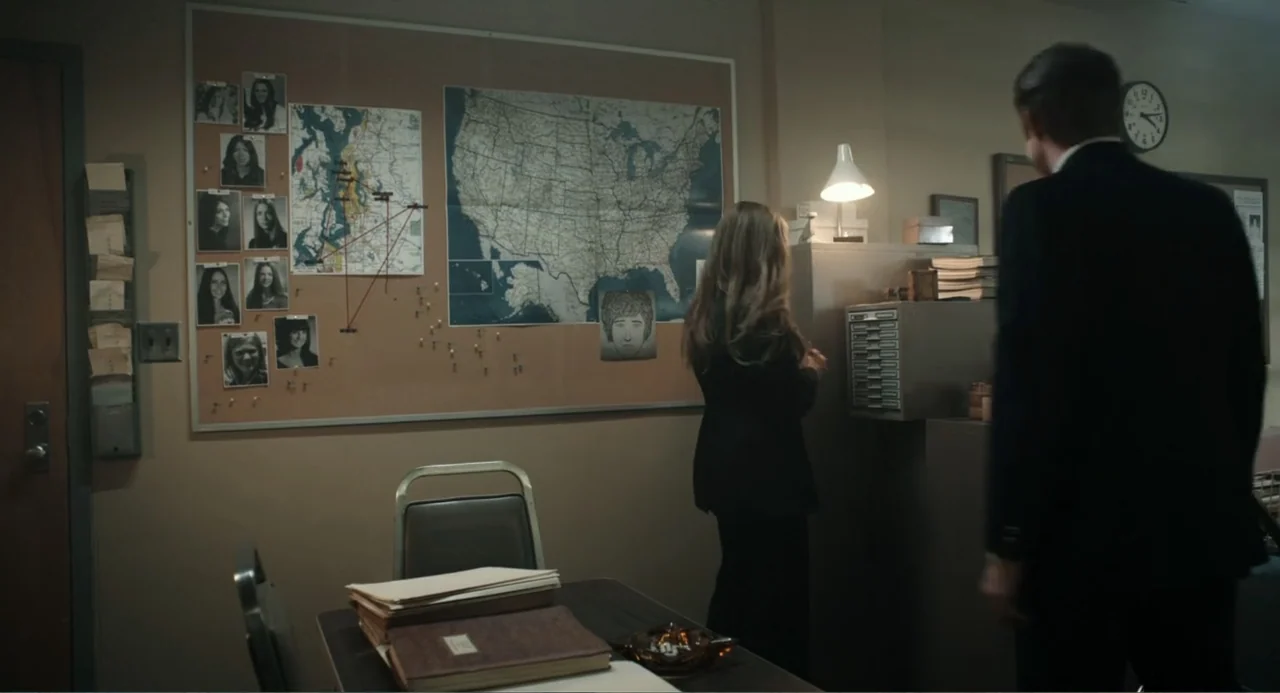 Ted Bundy: American Boogeyman (2021) movie still: medium — A 1970s style office features a large cork board with maps and photos. Two investigators…