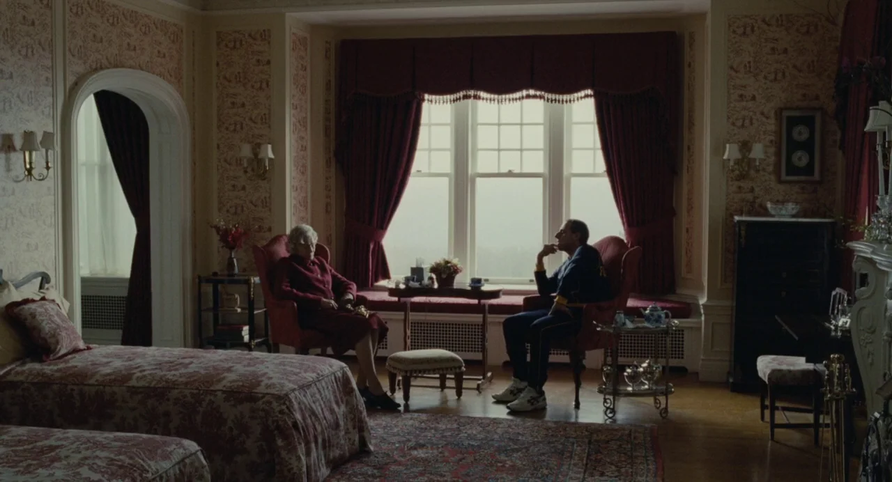 Foxcatcher (2014) movie still: wide — A traditional luxury hotel room features patterned wallpaper and antique furniture near a window. An elderly…