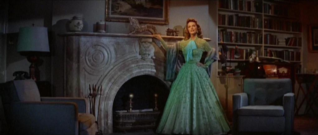 The Girl Can’t Help It (1956) movie still: fullbody — A formal library featuring a marble fireplace and tall, full bookshelves at night. A woman…