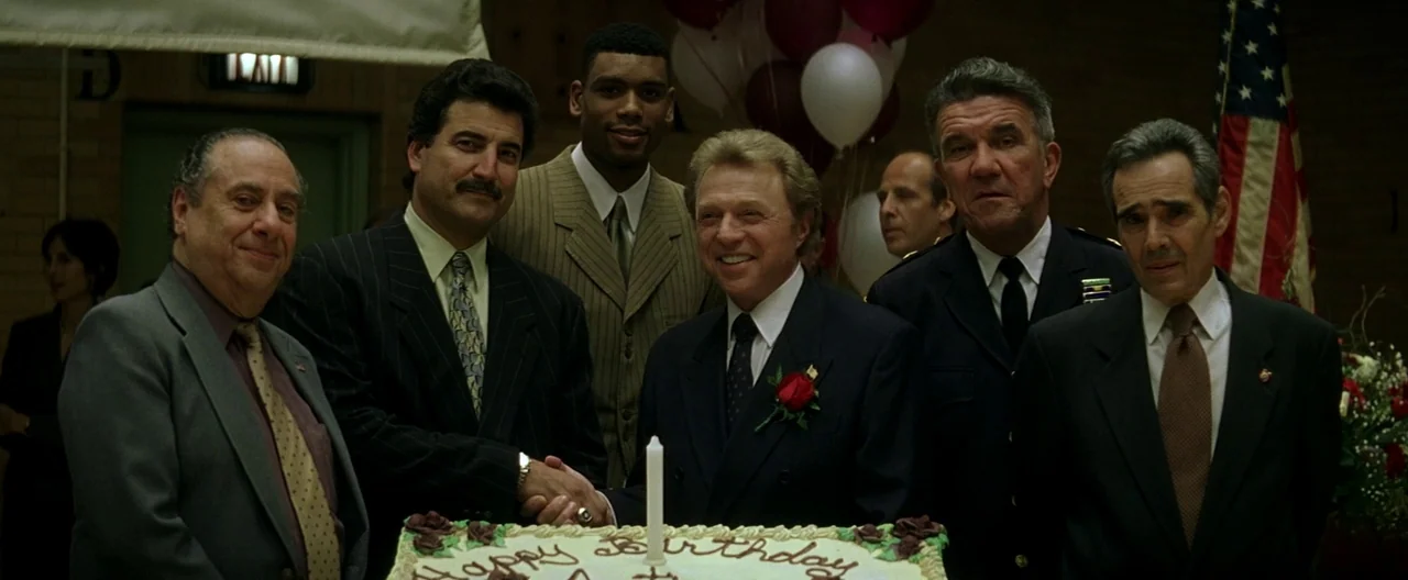 The Yards (2000) movie still: medium — A banquet hall interior features brick walls and birthday balloons in the background. Six men in formal suits…