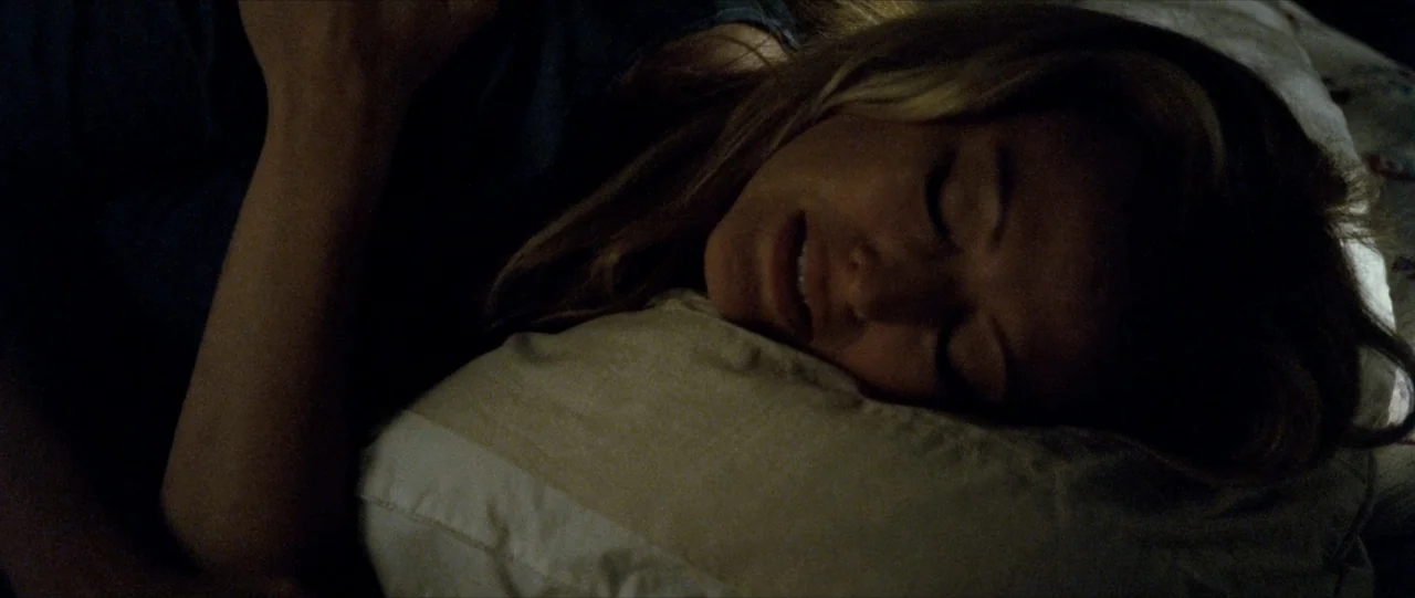 The Haunting in Connecticut (2009) movie still: closeup — A dimly lit indoor bedroom setting at night featuring a person sleeping. A young woman…