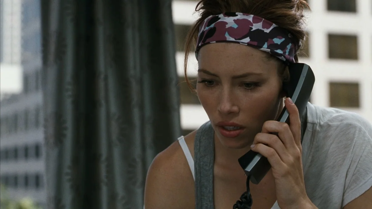 F Valentine's Day (2026) movie still: closeup — An interior space with a window looking out onto a city office building. A woman with a headband…