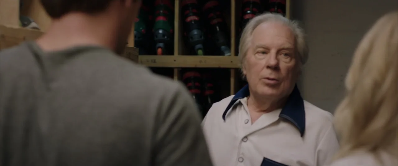 Playing God (2021) movie still: medium — A bowling alley rental desk features rows of bowling shoes stored on wooden shelves. An older man with gray…