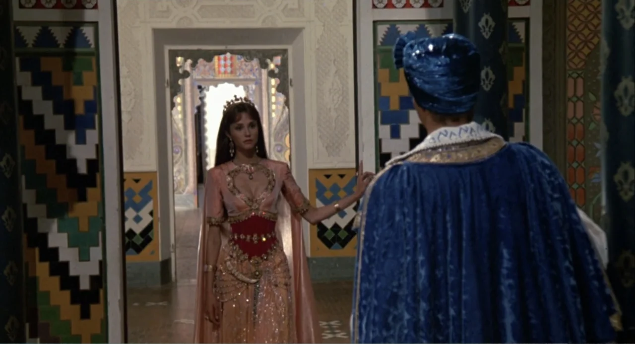 Hercules (1983) movie still: fullbody — A palace corridor with ornate geometric tile walls and arched doorways. A woman wearing an embellished dress…