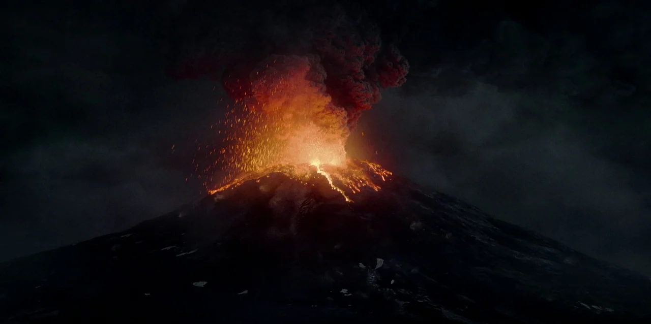 The Northman (2022) movie still: establishing — A dark, massive volcano peak dominates the frame under a thick, ash-filled night sky. An eruption…