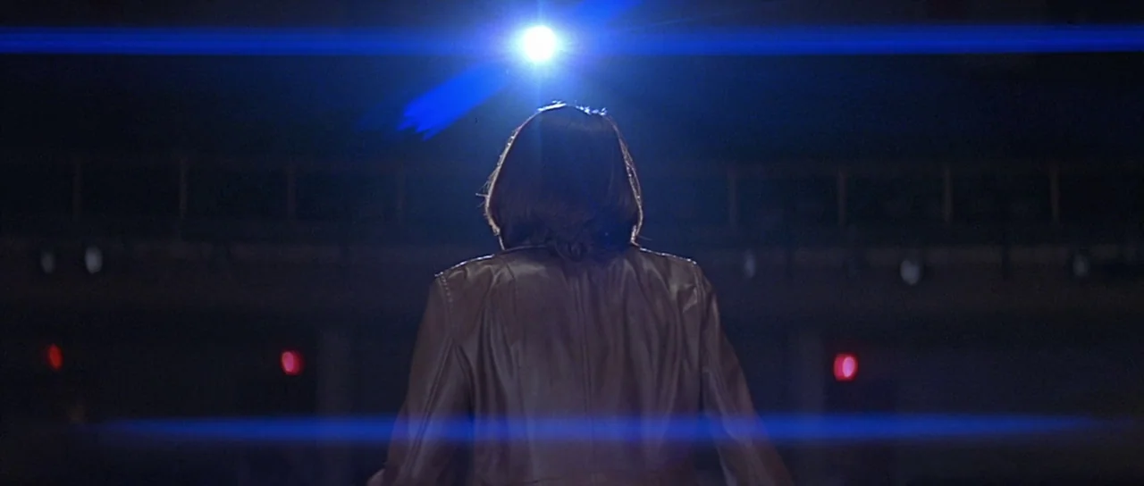 Scream 2 (1997) movie still: medium — An auditorium interior with a single overhead spotlight shining down from the darkness. A woman in a brown…