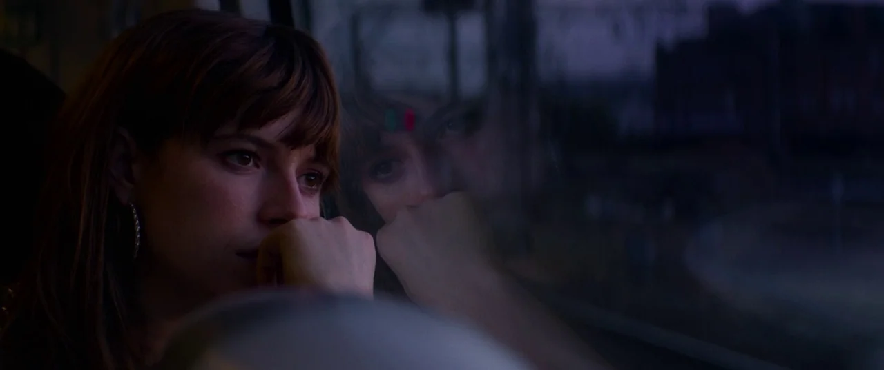 Wild Rose (2018) movie still: closeup — A woman looks out from the interior of a train at dusk. Her reflection appears faintly in the darkened glass…