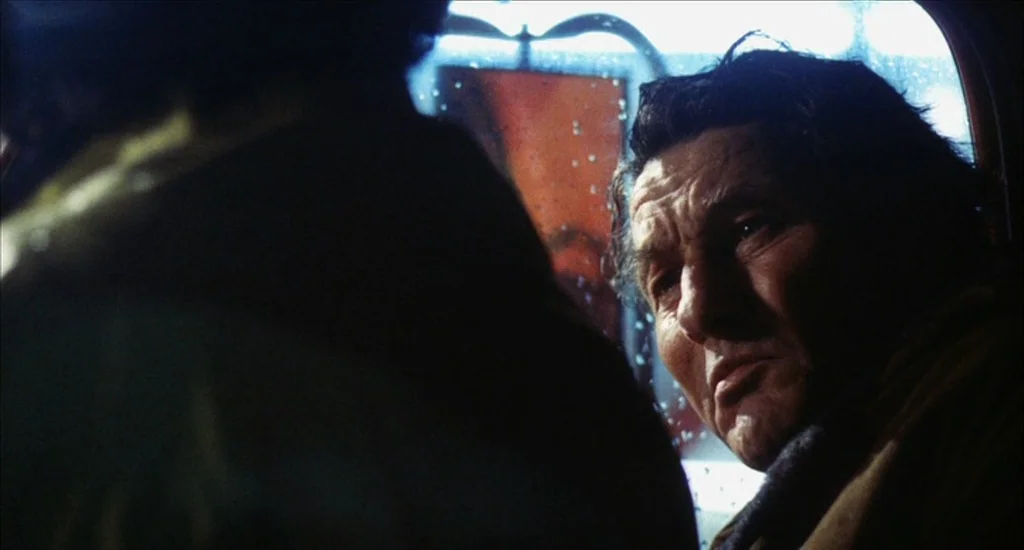 A Woman Under the Influence (1974) movie still: closeup — The interior of a car at night with raindrops visible on the glass window. An elderly man…