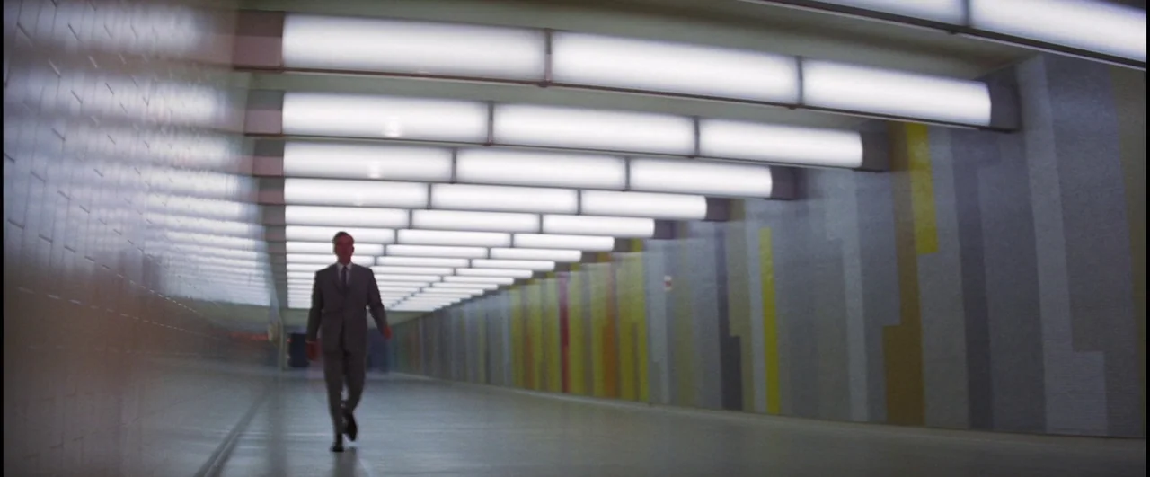 Point Blank (1967) movie still: wide — A long, brightly lit pedestrian tunnel features tiled walls with vertical yellow and grey patterns. A lone…
