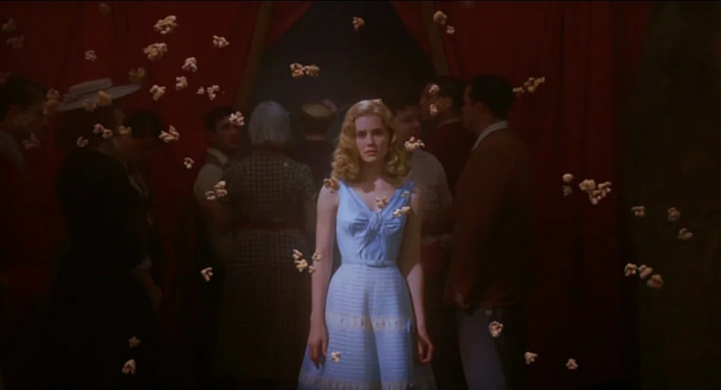 Big Fish (2003) movie still: medium — A dimly lit indoor theater lobby features heavy dark red curtains in the background. A woman in a blue dress…