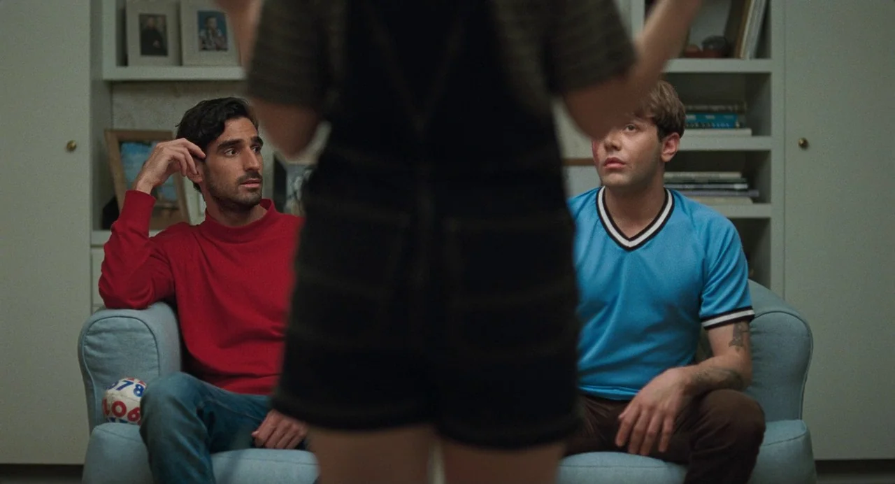 Matthias & Maxime (2019) movie still: medium — A living room interior features built-in white shelves filled with books and framed photos. Two men…