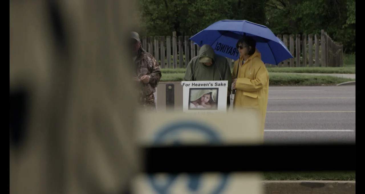 Abortion: Stories Women Tell (2016) movie still: medium — A roadside area with a wooden fence and trees in the background under daylight. Three…