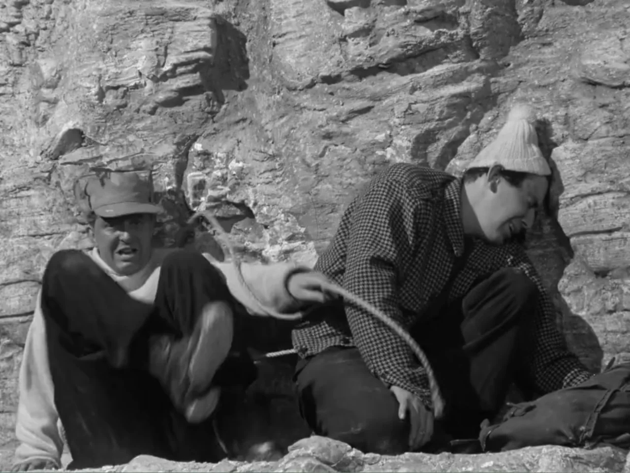 The Crawling Eye (1958) movie still: medium — Two men sit on a rugged stone ledge against a steep cliff face. The men are tethered together by a…