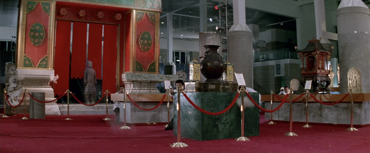 Rush Hour (1998) movie still: wide — A museum gallery features ornate Chinese architectural gates, red carpeting, and decorative stone pedestals. A…