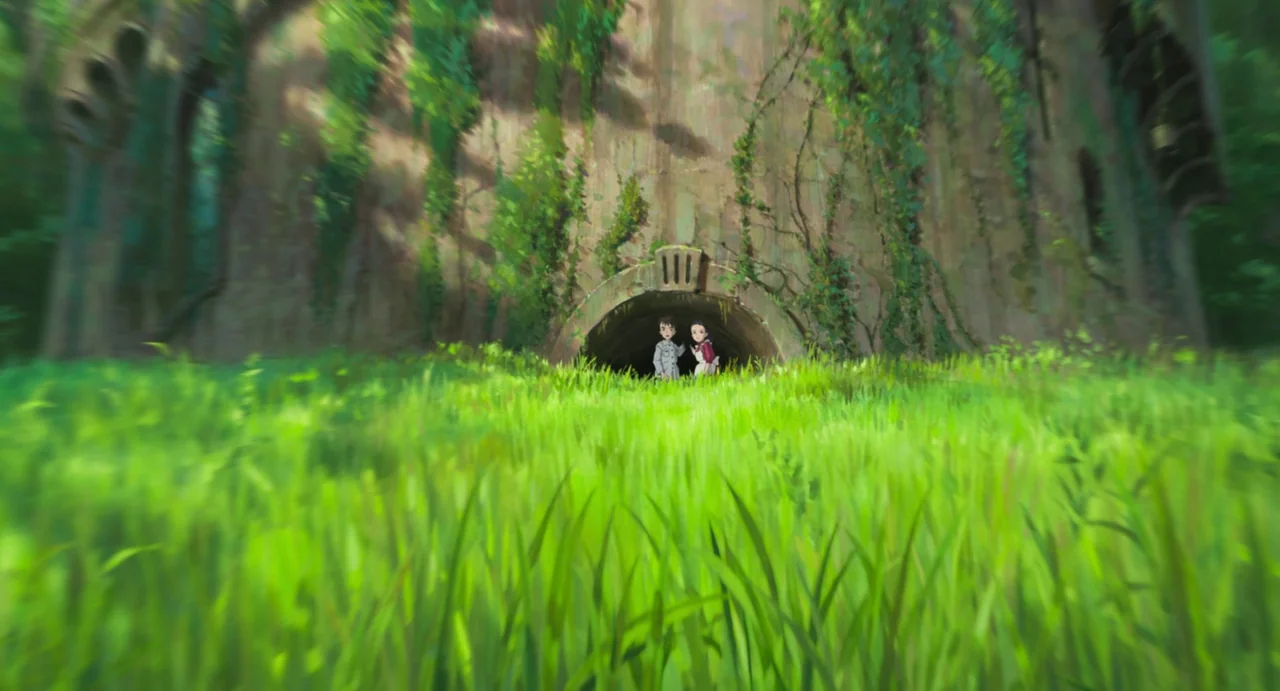 The Boy and The Heron (2023) movie still: wide — A wide, lush green meadow features a large ivy-covered stone structure with a tunnel. Two young…