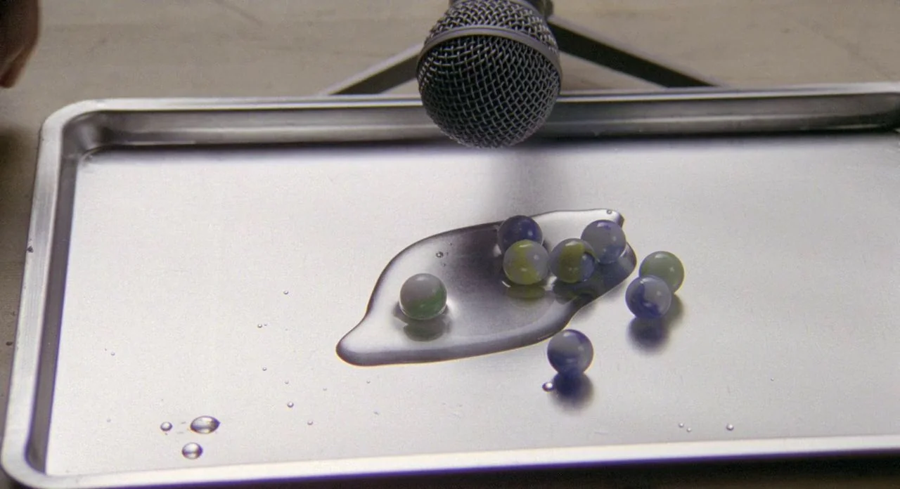 The Shout (1978) movie still: closeup — A metal tray holds a small pool of water and several spherical marbles. A microphone is suspended directly…