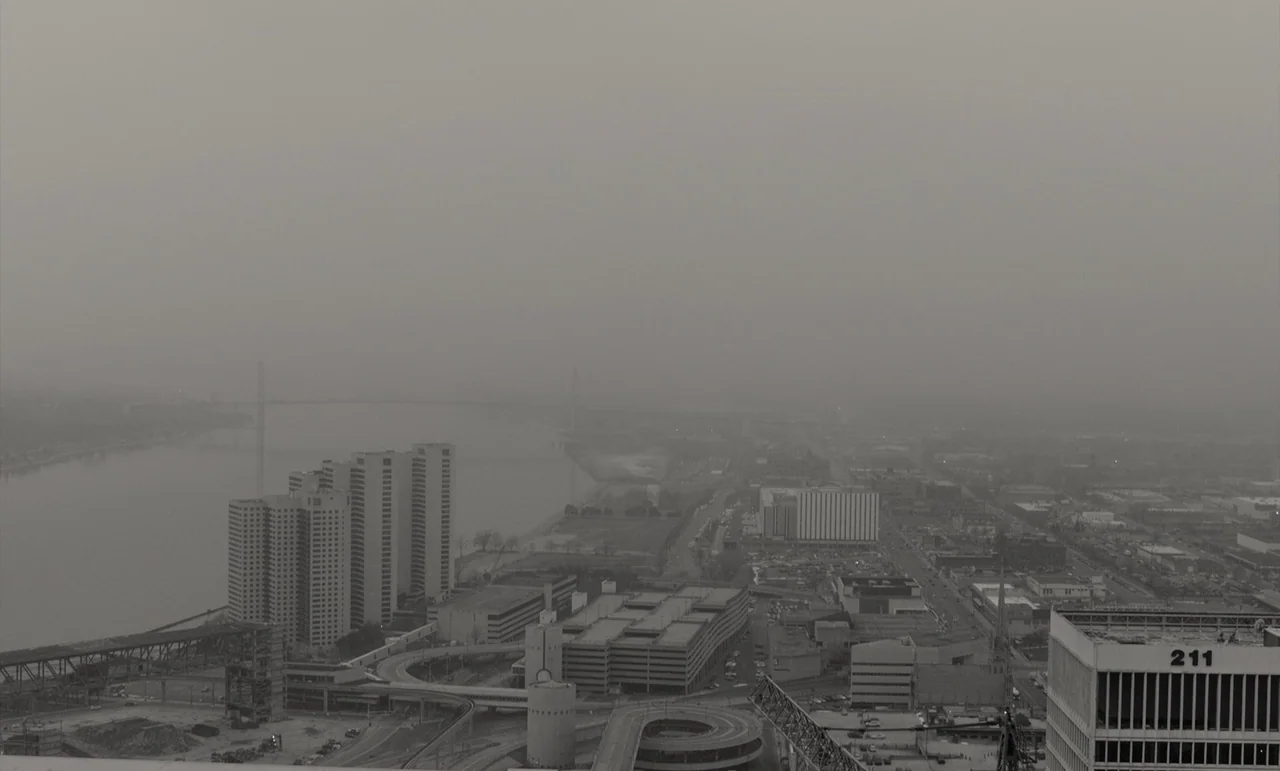 C’mon C’mon (2021) movie still: establishing — An aerial view of a sprawling urban industrial landscape partially obscured by dense fog. Tall…
