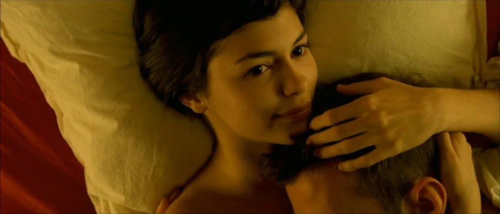 Amelie (2001) movie still: closeup — A close-up view of two people lying together on a vibrant red bedsheet. The woman rests her head on a white…