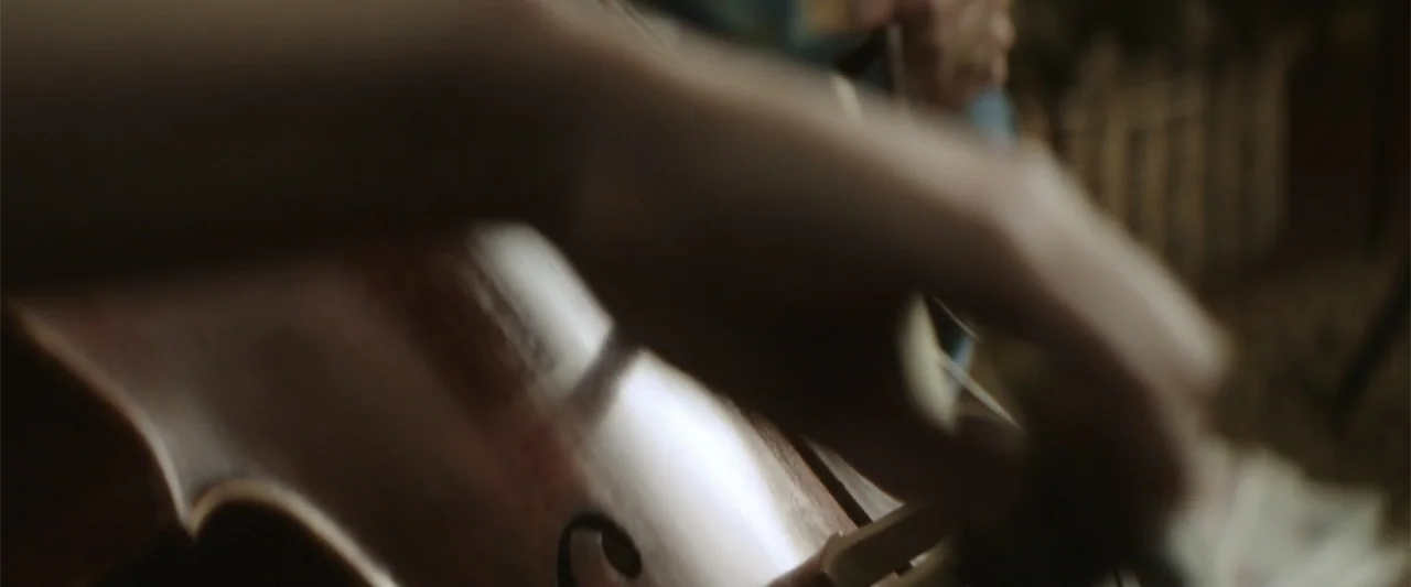 If I Stay (2014) movie still: closeup — An interior space contains a large wooden string instrument in the foreground. Blurred hands manipulate the…