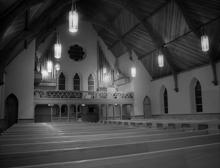 Carnival of Souls (1962) movie still: establishing — A spacious church interior features rows of wooden pews leading toward an organ gallery. The…